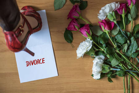 Woman legs in red high heel shoes standing on paper with word divorce on a floor with withered flowers. Heart broken concept.の写真素材