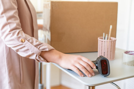 Female owner of start up small business using barcode scanner scanning retail drop shipping package postal parcel bar code. Warehouse worker.の写真素材