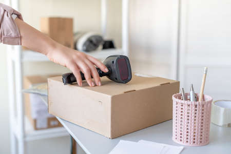 Woman employee of post office scanning parcel using barcode scanner to confirm sending customer. Home delivery service.の写真素材