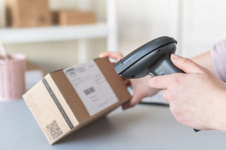 Female owner of start up small business using barcode scanner scanning retail drop shipping package postal parcel bar code. Warehouse worker.の写真素材