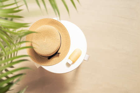 Sunscreen for protection skin and straw hat on the white table on the sandy beach in the palm tree forest. Summer vocation. Top view. Copy spaceの写真素材