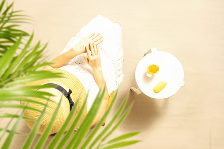 Alone woman applying sunscreen for protection skin sitting near sandy beach table with orange juice....
