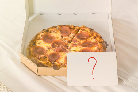 Open box of pizza on the big bed and card with question mark. Conceptの写真素材