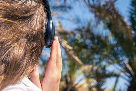 Back view on the girl in the headphones listening music walks in the palm forest. Seychelles islands