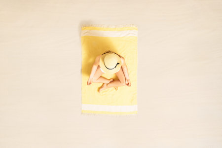 Woman in bikini meditates and relaxation in lotus pose sitting and sunbathing on yellow beach towel. Yoga. Summer vacation. Top, aerial viewの写真素材
