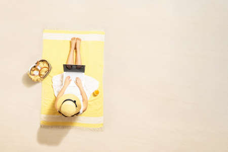 Woman with laptop, bag and headphones drinking juice sitting on the beach towel and enjoying summer vacation. Aerial view. Copy spaceの写真素材