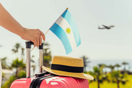 Woman with pink suitcase and Argentina flag standing on passengers ladder and getting out of airplane opposite sea coastline with palm trees.の写真素材