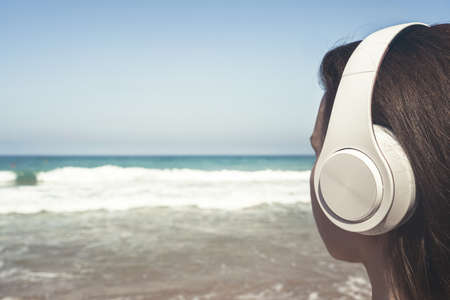 Alone woman on a beach in headphones listen music looking on the sea. Female relaxation at summer vacation. Back viewの写真素材