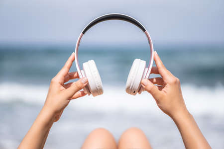Woman hands with headphones on a beach and sea coastline.の写真素材