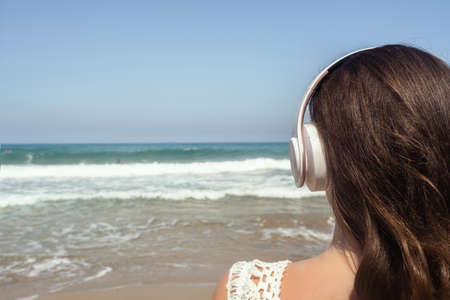 Alone woman on a beach in headphones listen music looking on the sea. Female relaxation at summer vacation. Back viewの写真素材