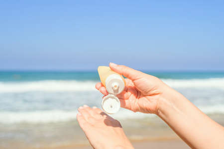 Woman applying sunscreen on skin of hand on a beach of coastline sea. Female relaxation at summer vacation. Back viewの写真素材