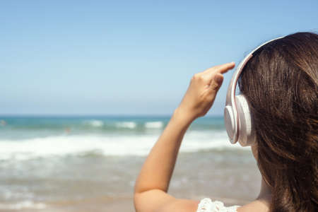 Alone woman on a beach in headphones listen music looking on the sea. Female relaxation at summer vacation. Back viewの写真素材
