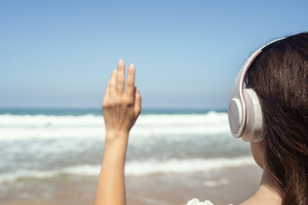 Alone woman in headphones waving hand and say goodbye to sea standing on a beach.