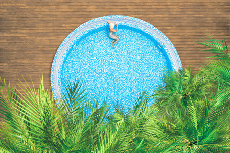 Young alone, beautiful sports woman in bikini and hat is swimming in swimming pool with palm trees....