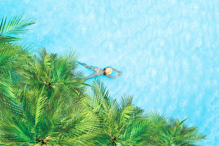 Top view of young woman in bikini and straw hat is swimming in transparent blue sea, lagoon under palm trees. Aerial, drone viewの写真素材