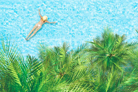 Top view of young woman in bikini and straw hat is swimming in transparent blue sea, lagoon under palm trees. Aerial, drone viewの写真素材
