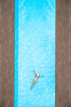 Young alone beautiful sports woman in bikini and hat is swimming in swimming pool. Aerial drone view from above. Tropical summer vacationの写真素材