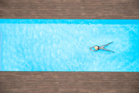 Young alone beautiful sports woman in bikini and hat is swimming in swimming pool. Aerial drone view from above. Tropical summer vacationの写真素材