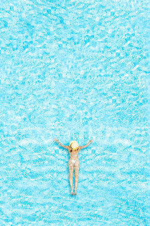 Young alone beautiful sports woman in bikini and hat is swimming in swimming pool. Aerial drone view...