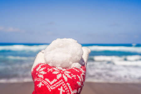 Woman hands in christmas gloves holding snowball on beach opposite sea wave. New yearの写真素材