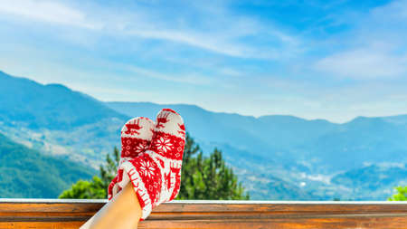 Woman in Christmas red socks, boots sits on a balcony in the mountainsの写真素材