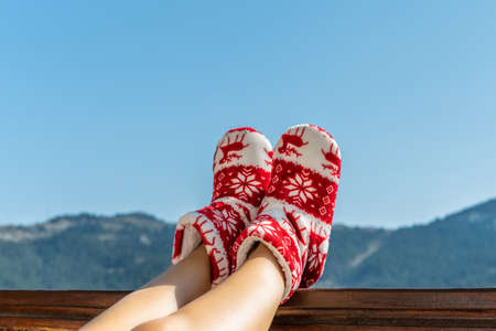oman in Christmas red socks, boots sits on a balcony in the mountains putting her feet on the wooden terrace railingの写真素材