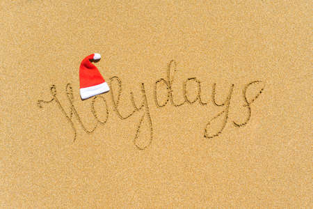 Painted holydays word on the beach sand with christmas hat. New year gift conceptの写真素材