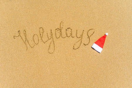 Painted holydays word on the beach sand with christmas hat. New year gift conceptの写真素材