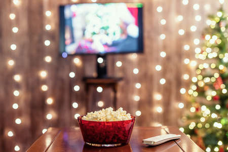 Christmas eve. Red bowl with popcorn. Remote control for tv on the table. Home cinema. Cropped, close upの写真素材
