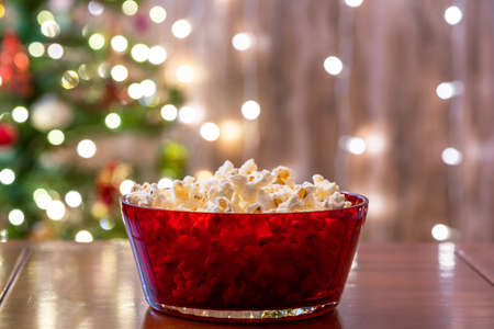 Christmas eve. Red bowl with popcorn on the table near christmas tree. Home cinema. Cropped, close upの写真素材