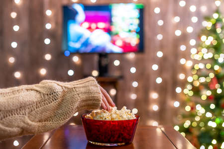 Christmas eve. Alone woman watching tv and eating popcorn. Home cinema. Cropped, close upの写真素材