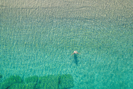 Young woman in a swimsuit and hat swimming in sea waves near the beach. View from above. Top, drone viewの写真素材