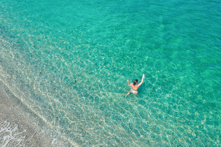 Young nude beautiful, sexy woman with naked breast taking off swimsuit standing in sea, ocean water. Summer. View from above. Top view, copterの写真素材
