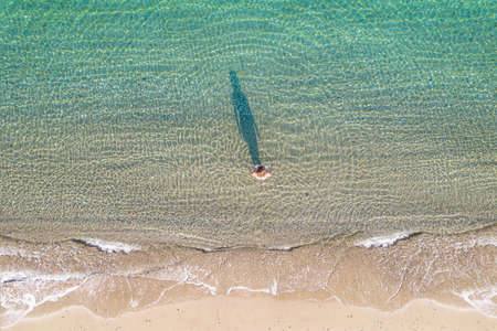 Young athletic woman in swimsuit walking barefoot on coast entering in sea on the sand beach. Summer. View from above. Top view, copterの写真素材
