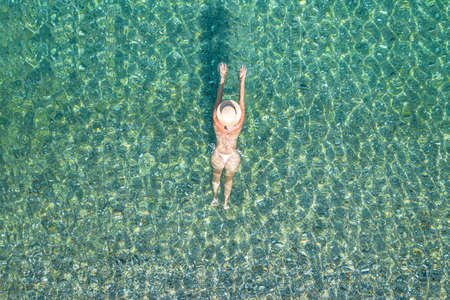 Young woman in a swimsuit and hat diving plunging and jumping on sea waves on the beach. View from above. Top, drone viewの写真素材