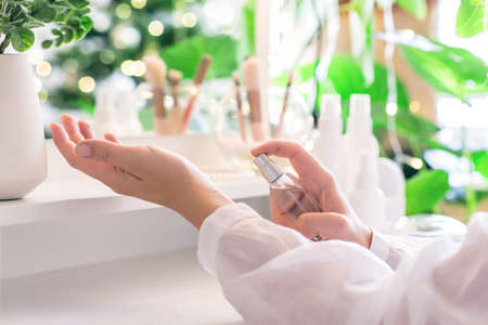 Woman applying perfume on her hand sitting near dressing table with make up accessories and table mirror. Self-Care.の写真素材