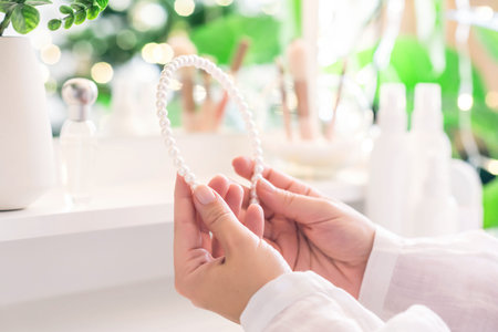 Woman puts on hair band, jewelry, pearl bracelets on the hand and sitting near dressing table with...
