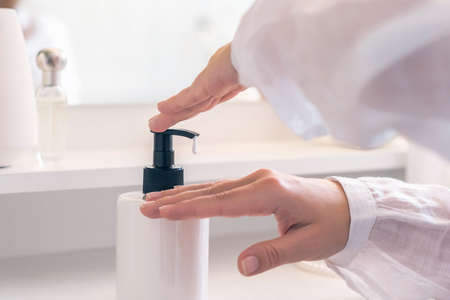 Woman applying daily cream on her hand sitting near dressing table with make up accessories and table mirror.の写真素材