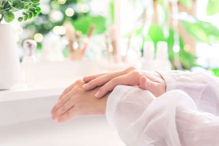 Woman applying daily cream on her hand sitting near dressing table with make up accessories. Reflection of christmas tree, light bulbs in table mirror.の写真素材