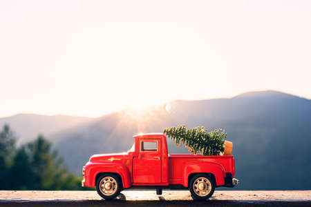 Red retro small car carrying christmas tree in the mountain in the sunbeams of sunrise. Winter holiday conceptの写真素材