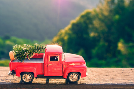 Red retro small car carrying christmas tree in the mountain. Winter holiday concept