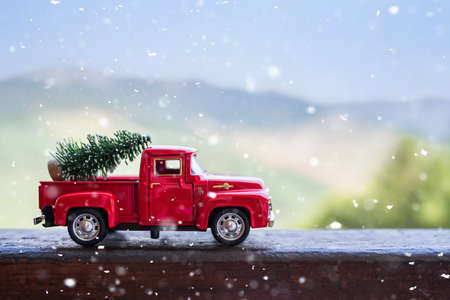 Red retro small car carrying christmas tree in the mountain in snowfall. Winter holiday conceptの写真素材