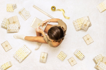 Female wrapping christmas gifts boxes for family sitting on fluffy snow-white carpet. Top view.の写真素材