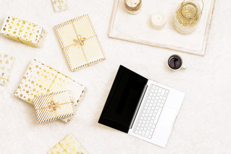 Christmas. Online shopping. Laptop among the many wrapped gifts in white gold wrapping paper on the...