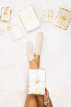 Female wrapping christmas gifts boxes for family sitting on fluffy snow-white carpet. Top view.Vertical ratioの写真素材