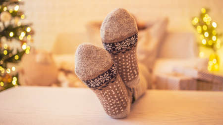 Woman sitting on couch near christmas tree. Female legs, feet in winter woolen socks putting on the table and relaxing after packing handmade gift boxes. Presents for family.の写真素材
