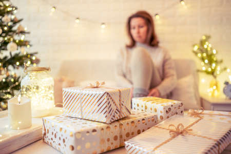 Woman sitting on couch near christmas tree. Female legs, feet in winter woolen socks putting on the table and relaxing after packing handmade gift boxes. Presents for family.の写真素材