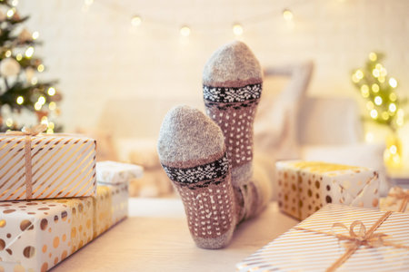 Woman sitting on couch near christmas tree. Female legs, feet in winter woolen socks putting on the...