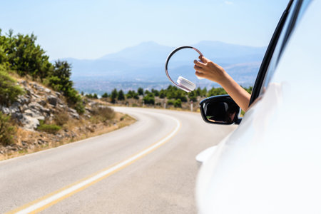 Woman driving a car holding headphones from the open window. Trip on the serpentine road in the mountains. Summer vacationの写真素材