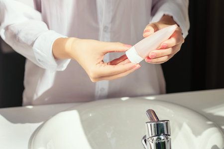 Woman applying cream after washing hands for protective and care dry skin near white sink in...